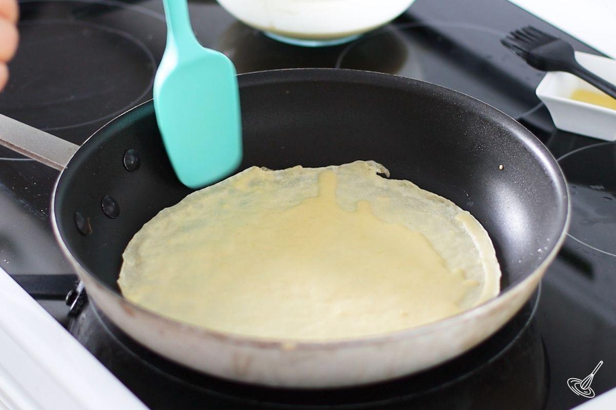 Someone using a rubber spatula to gently flip a Pâte à Crêpes.