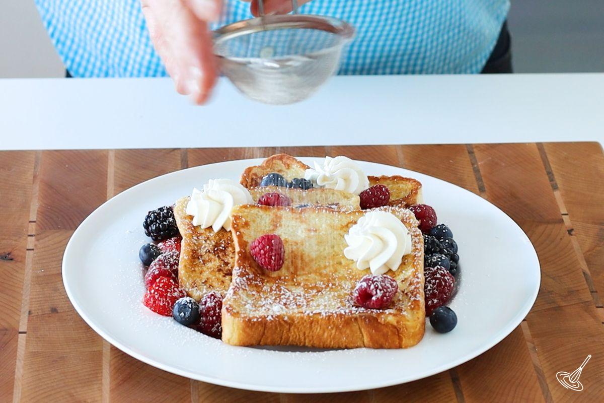 Someone dusting icing sugar on a place of cinnamon vanilla french toast.