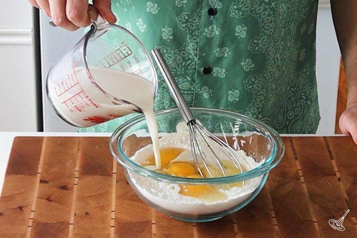 Someone pouring milk in a bowl of Pâte à Crêpes.