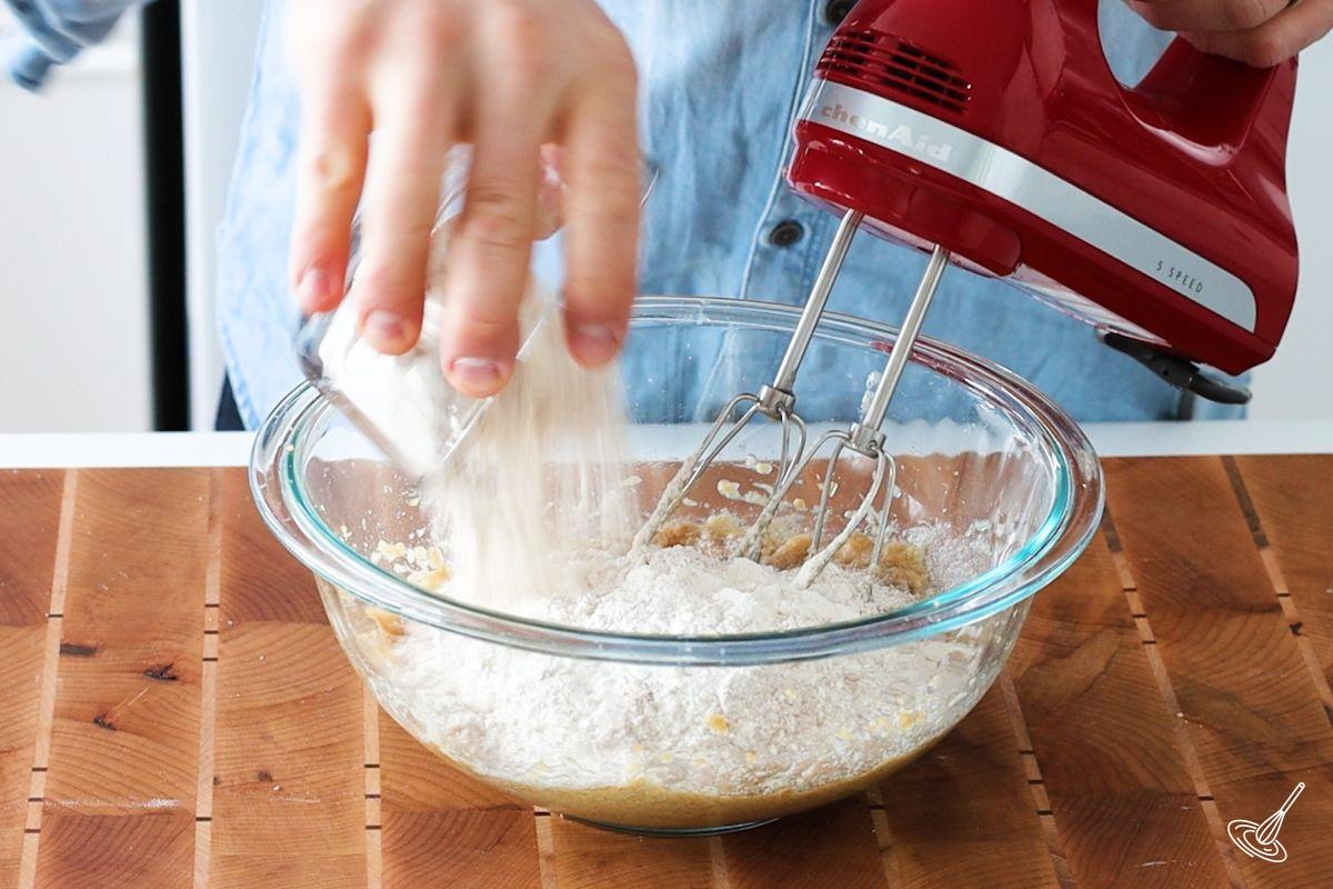 Someone adding dry ingredients to wet ingredients in a large bowl.