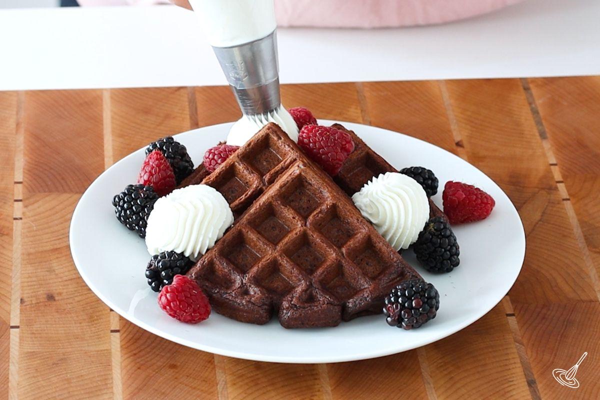 Someone piping whipping cream on top of Chocolate Cottage Cheese Waffles.