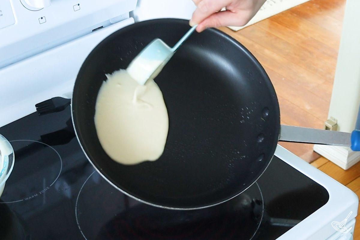 Someone pouring Pâte à Crêpes batter into a frying pan. 