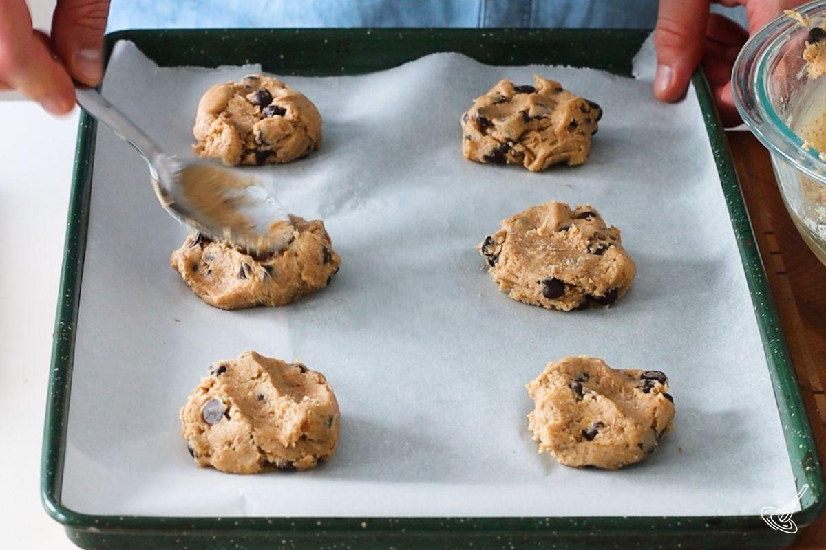 Someone using the back of a spoon to press down Vegan Banana Chocolate Chip Cookies before they go into the oven.