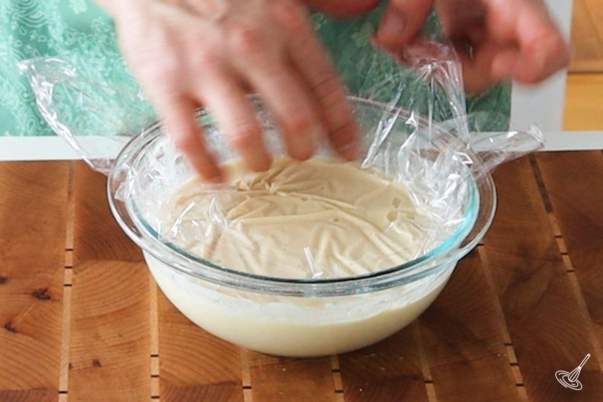 Someone placing plastic wrap directly on the top of Pâte à Crêpes.
