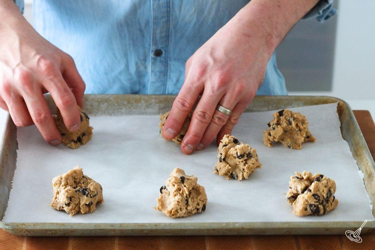 Someone placing balls of cookie dough on a baking tray.