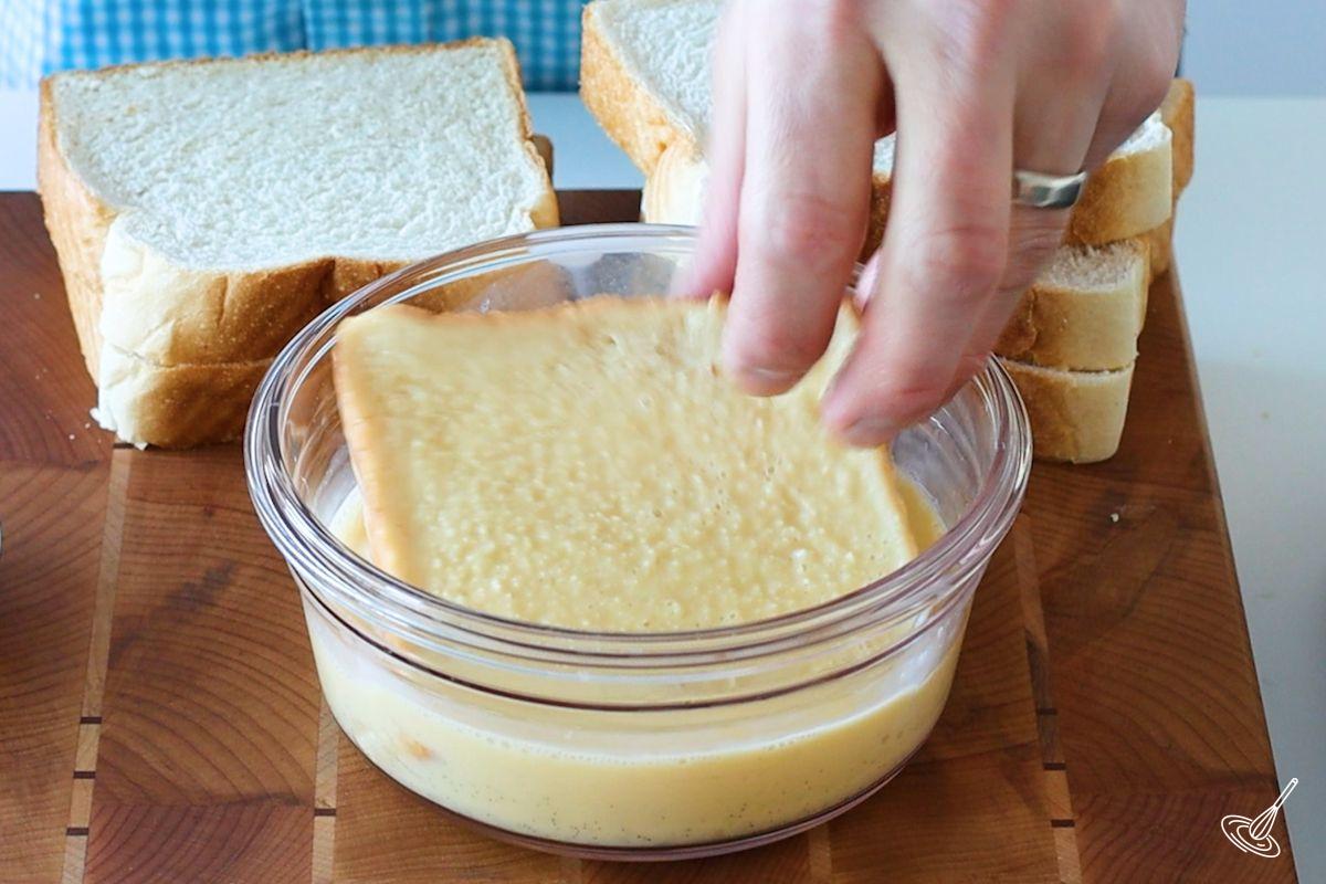 Someone dipping a slice of bread into an egg mixture.
