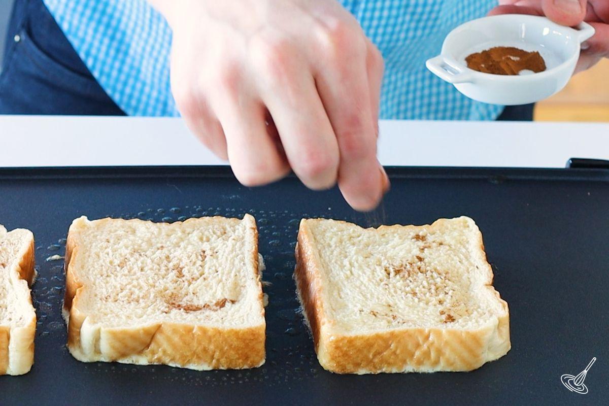 Someone sprinkling cinnamon on top of French toast. 