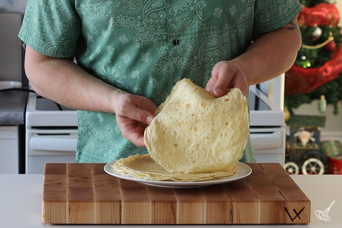 Someone placing a cooked Crêpe in a stack on a plate.