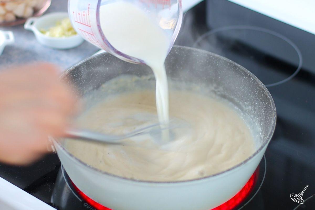 Someone whisking in milk into a sauce pan. 