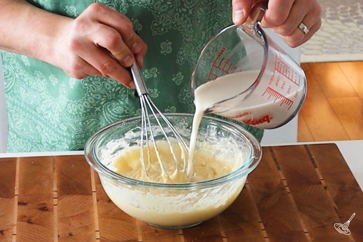 Someone slowly pouring and whisking in milk in Pâte à Crêpes.