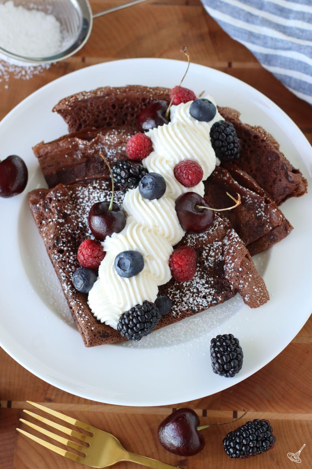 Chocolate French Crepes on a plate with whipped cream and berries.