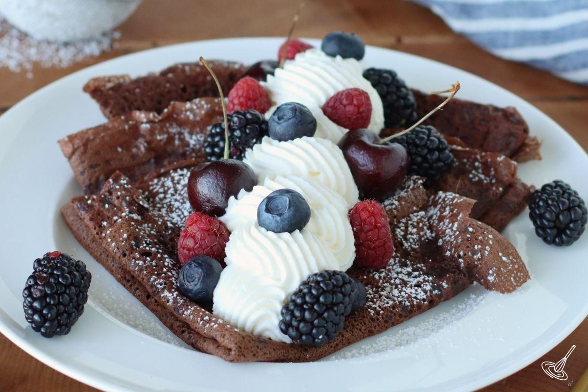 Chocolate French Crepes on a plate with whipping cream and berries.