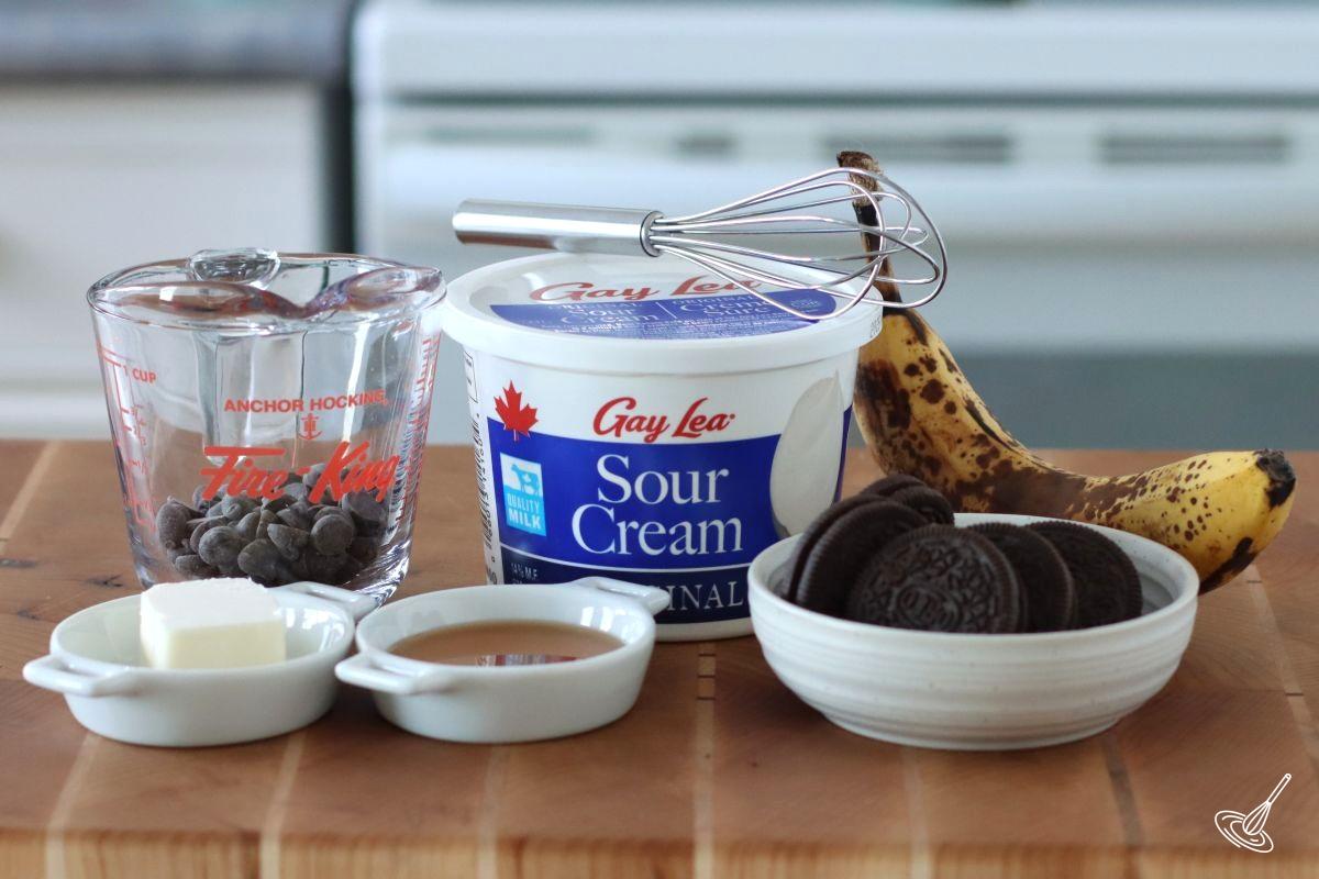 Ingredients to make a chocolate tart including; sour cream, cookies, and chocolate chips.