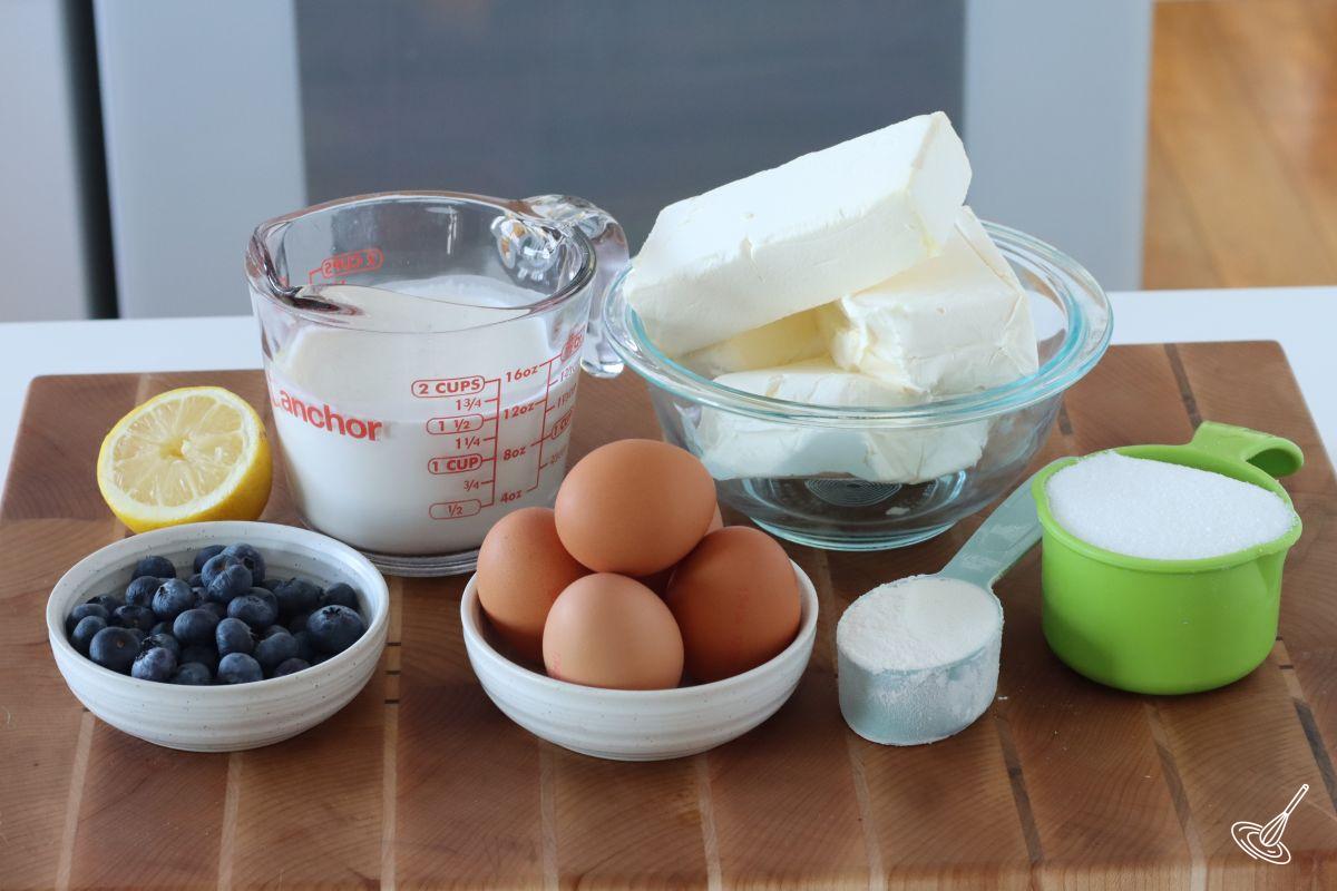 Ingredients to make a cheesecake, including cream cheese, heavy cream, sugar, and eggs.