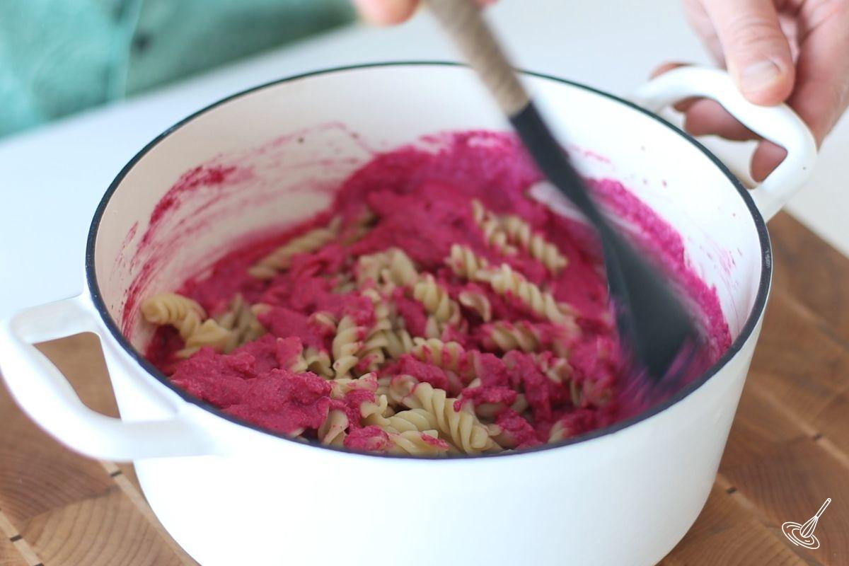 Someone stirring cooked pasta into the roasted beet and feta sauce.