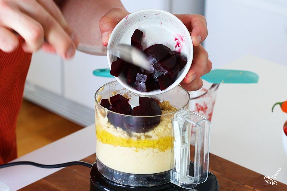 Someone adding cubed beets to a food processor with hummus.