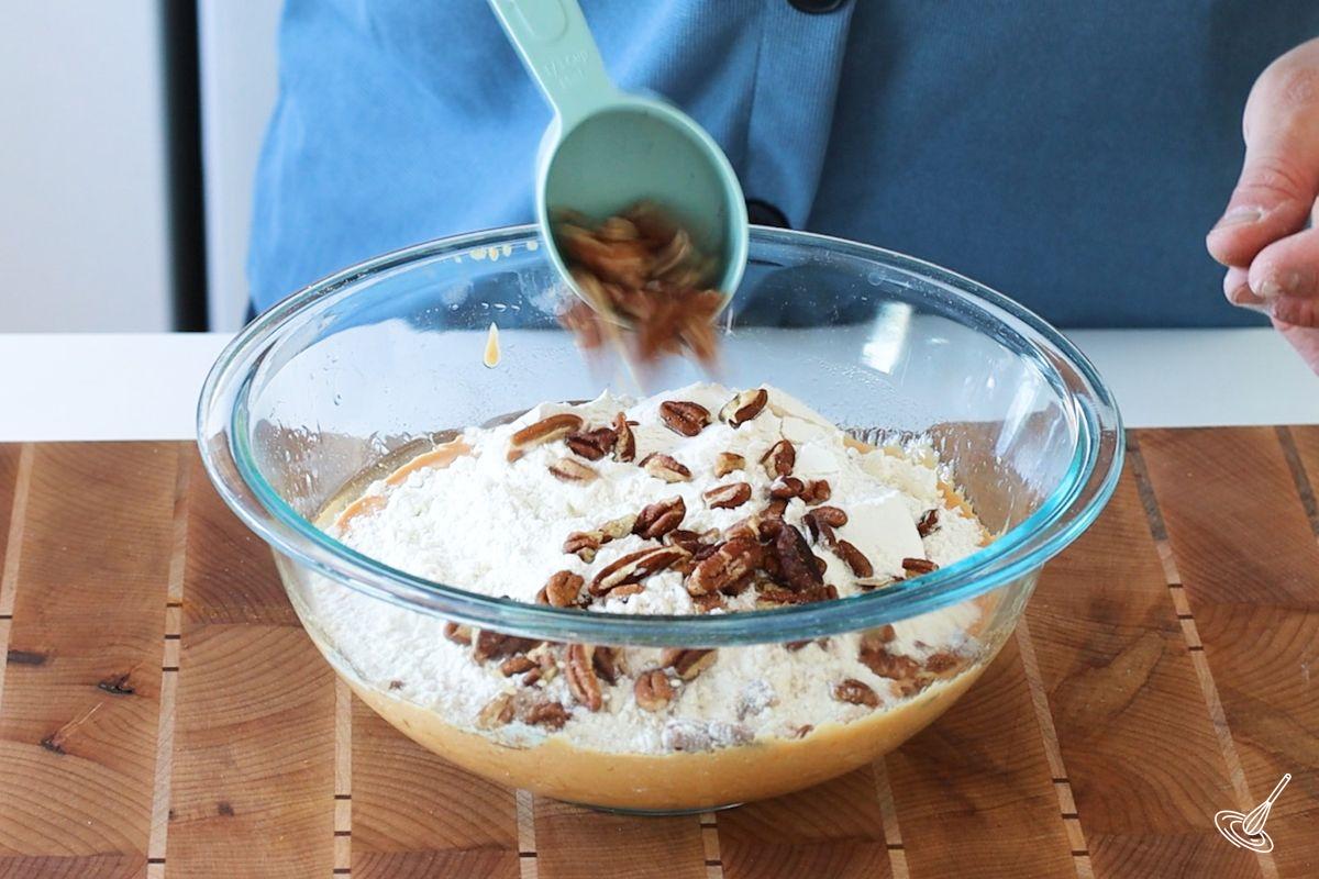 Someone adding chopped pecans to a large bowl of pumpkin cottage cheese muffins batter.