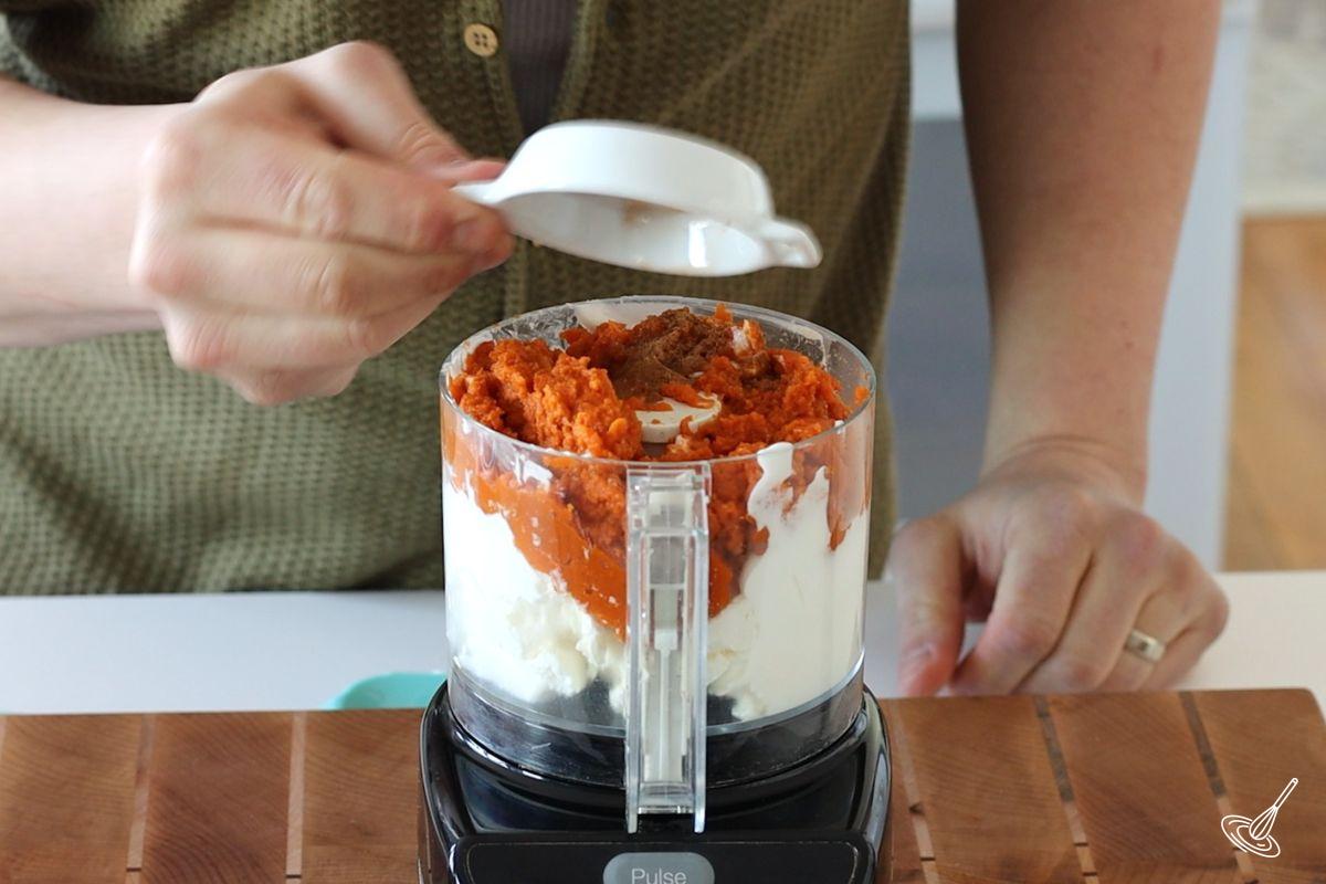 Someone adding spiced to a bowl of the food processor. 