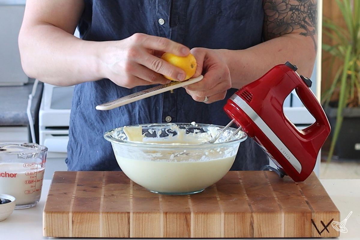 Someone adding lemon zest to a bowl of cheesecake batter. 