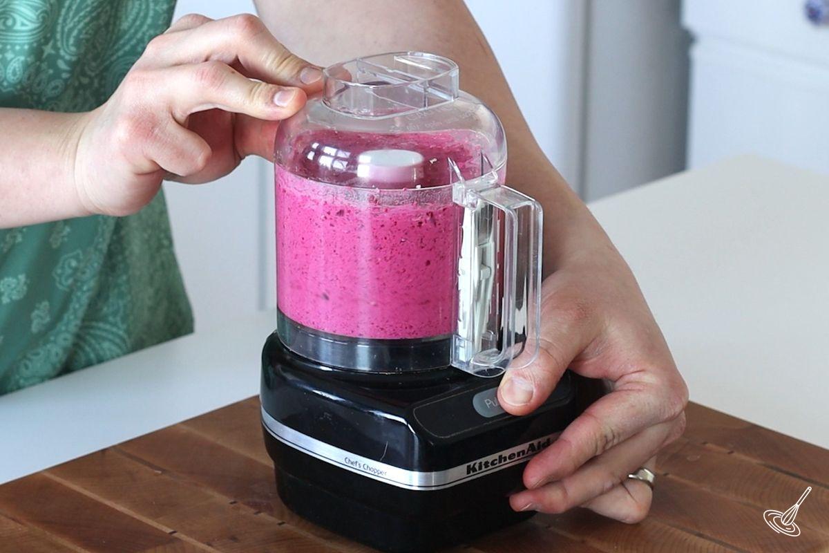 Someone blending beets and feta together in a food processor. 