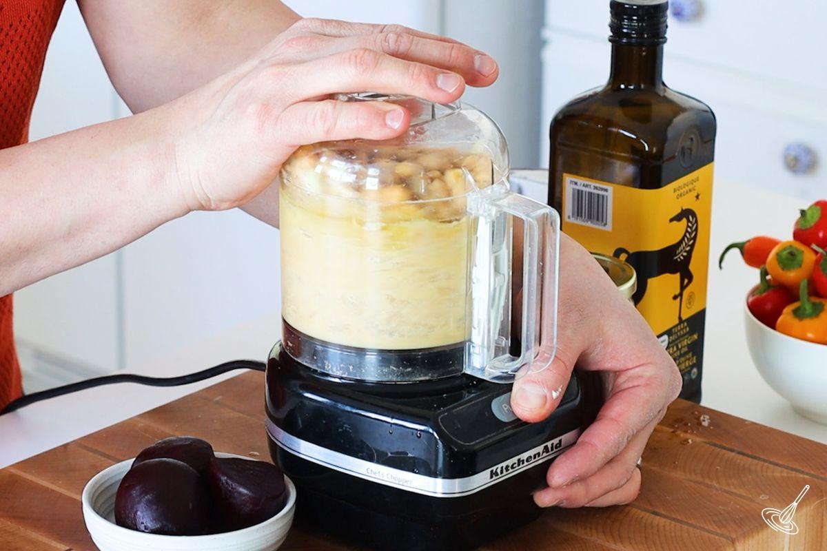 Someone using a food processor to make lemon beet hummus. 