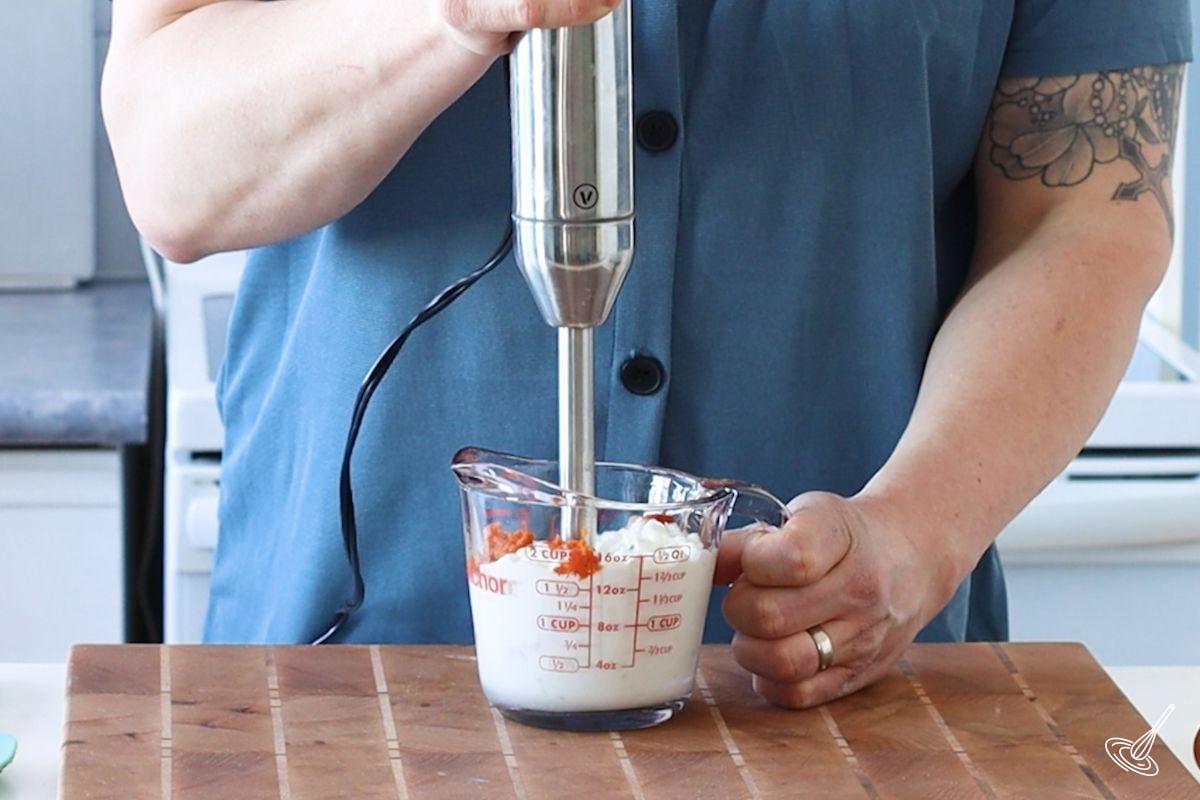Someone using a stick blender to puree cottage cheese and pumpkin. 