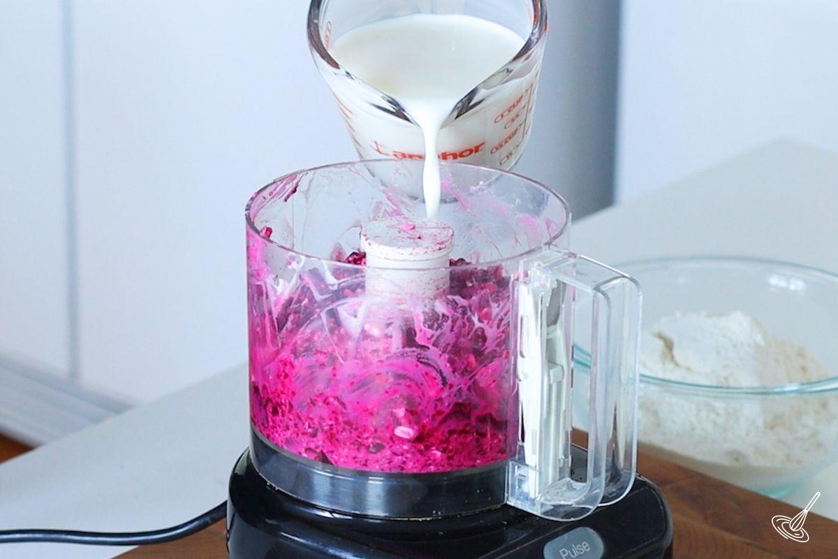 Someone pouring milk in a food processor with cottage cheese and beets.