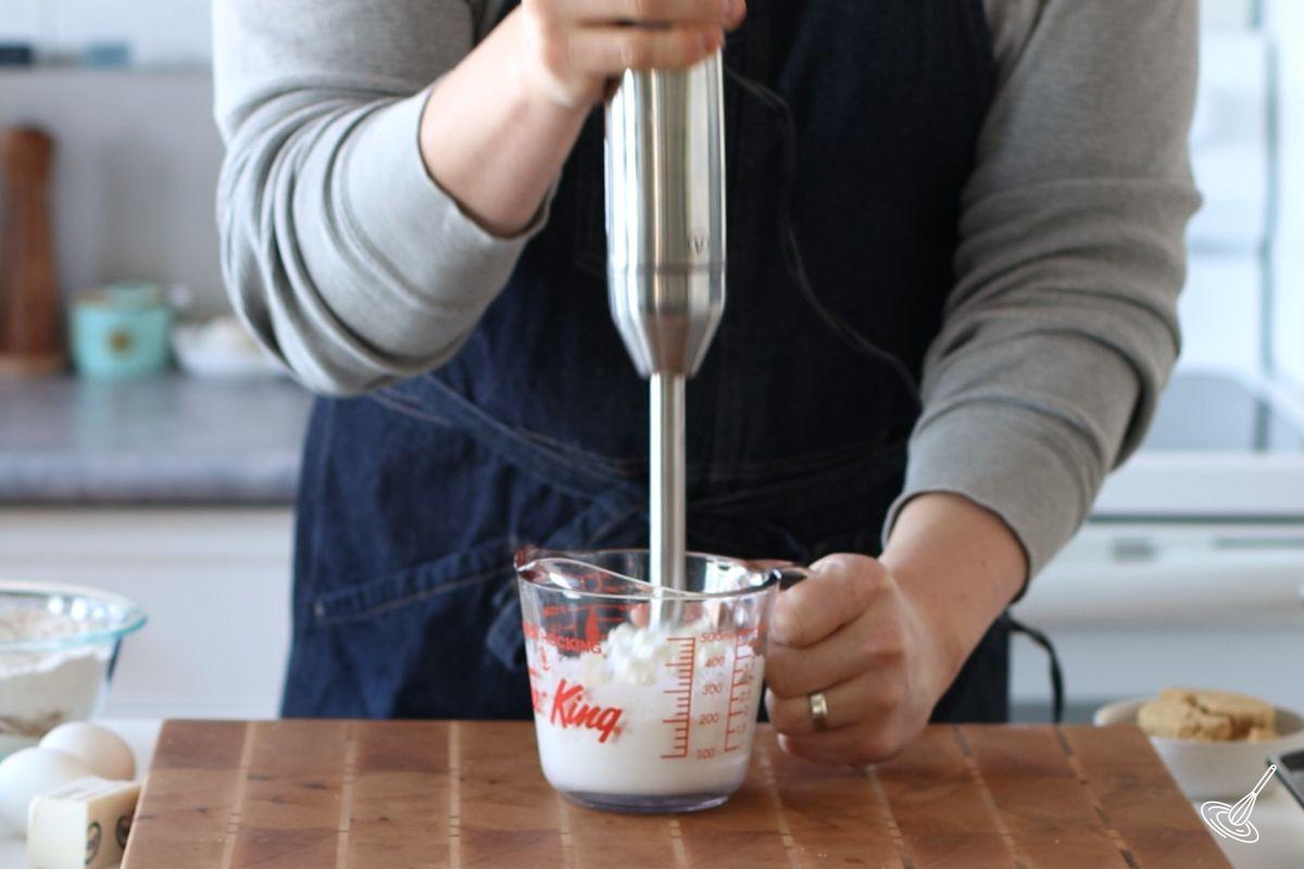 Someone using an immersion blender to puree cottage cheese. 