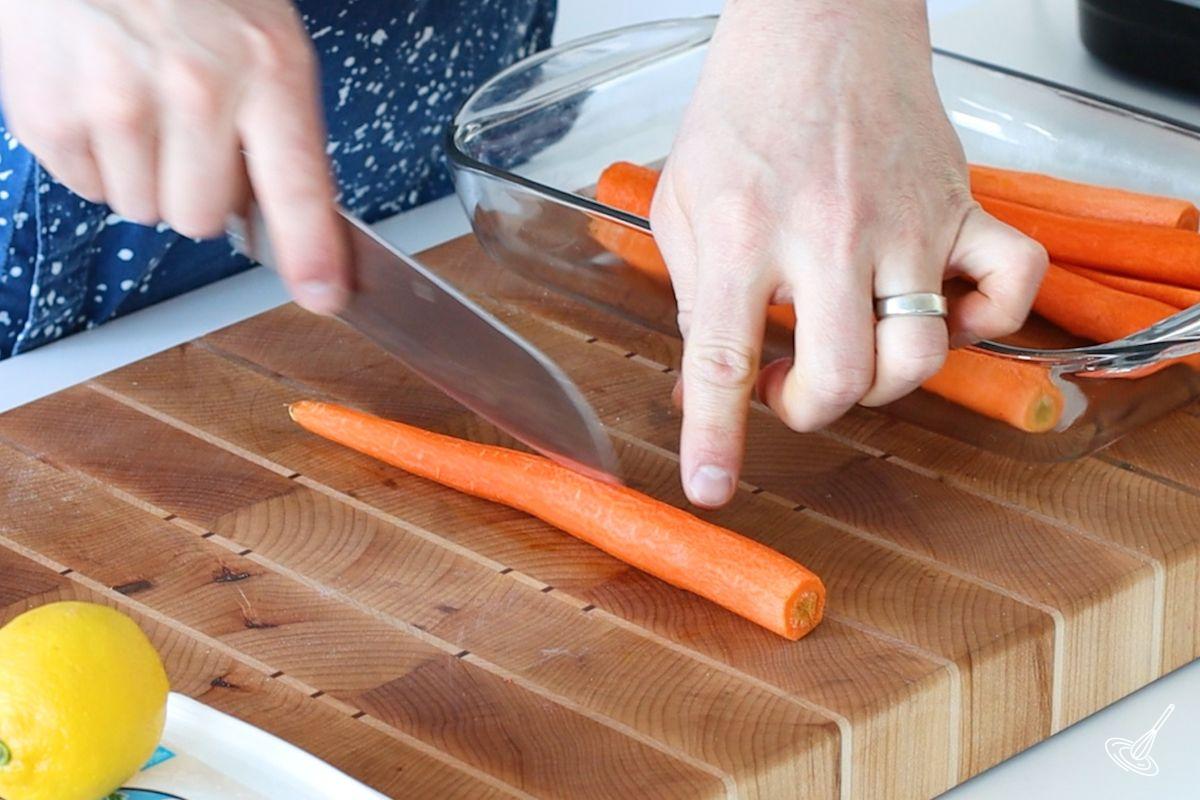 Someone cutting a peeled carrot in half lengthwise. 