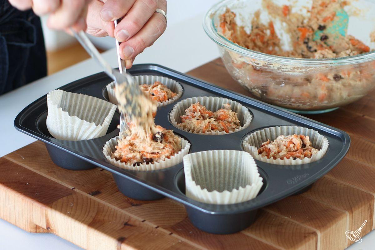 Someone using 2 spoons to divide the batter into 6 muffin cavities.