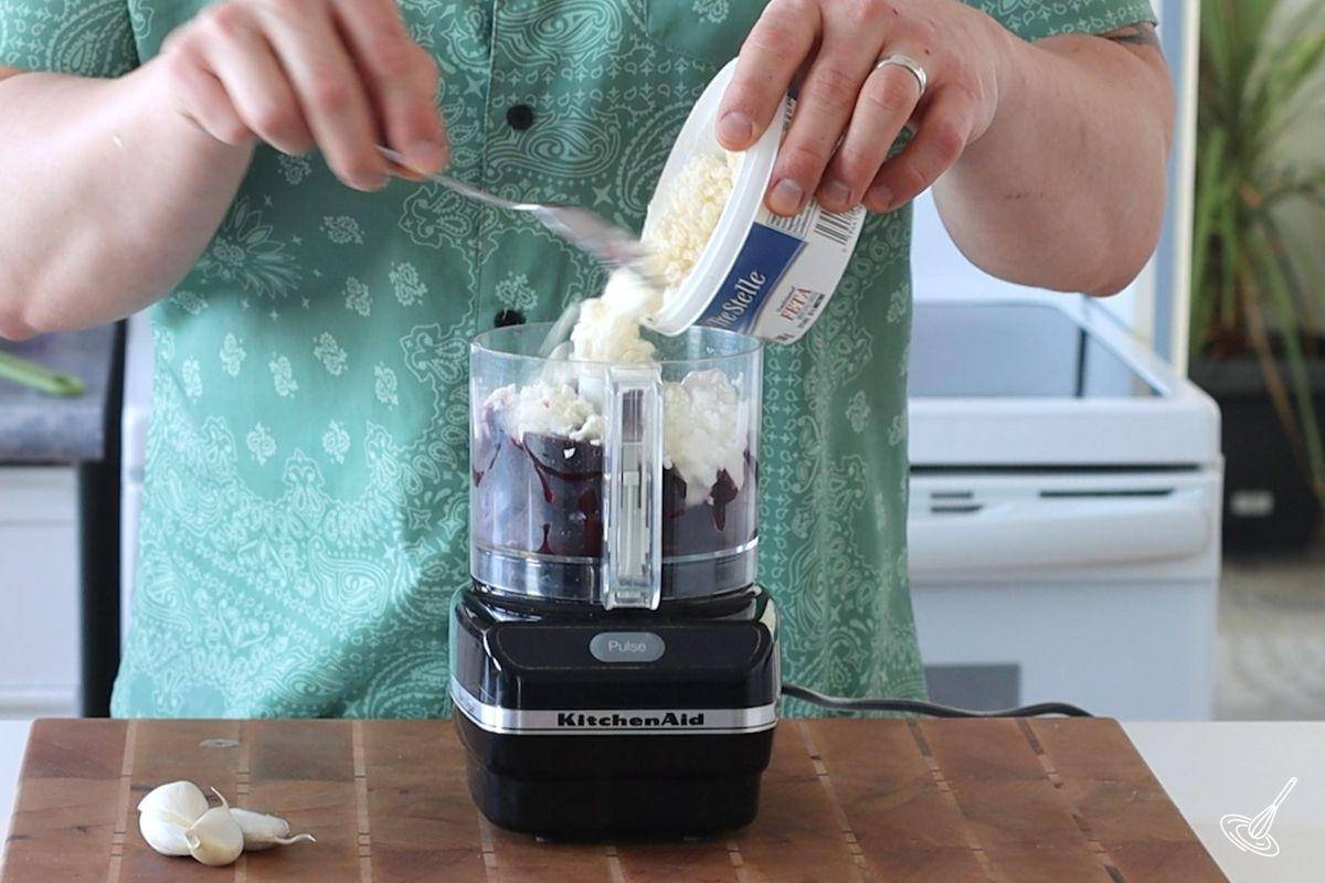 Someone adding feta to a food processor.