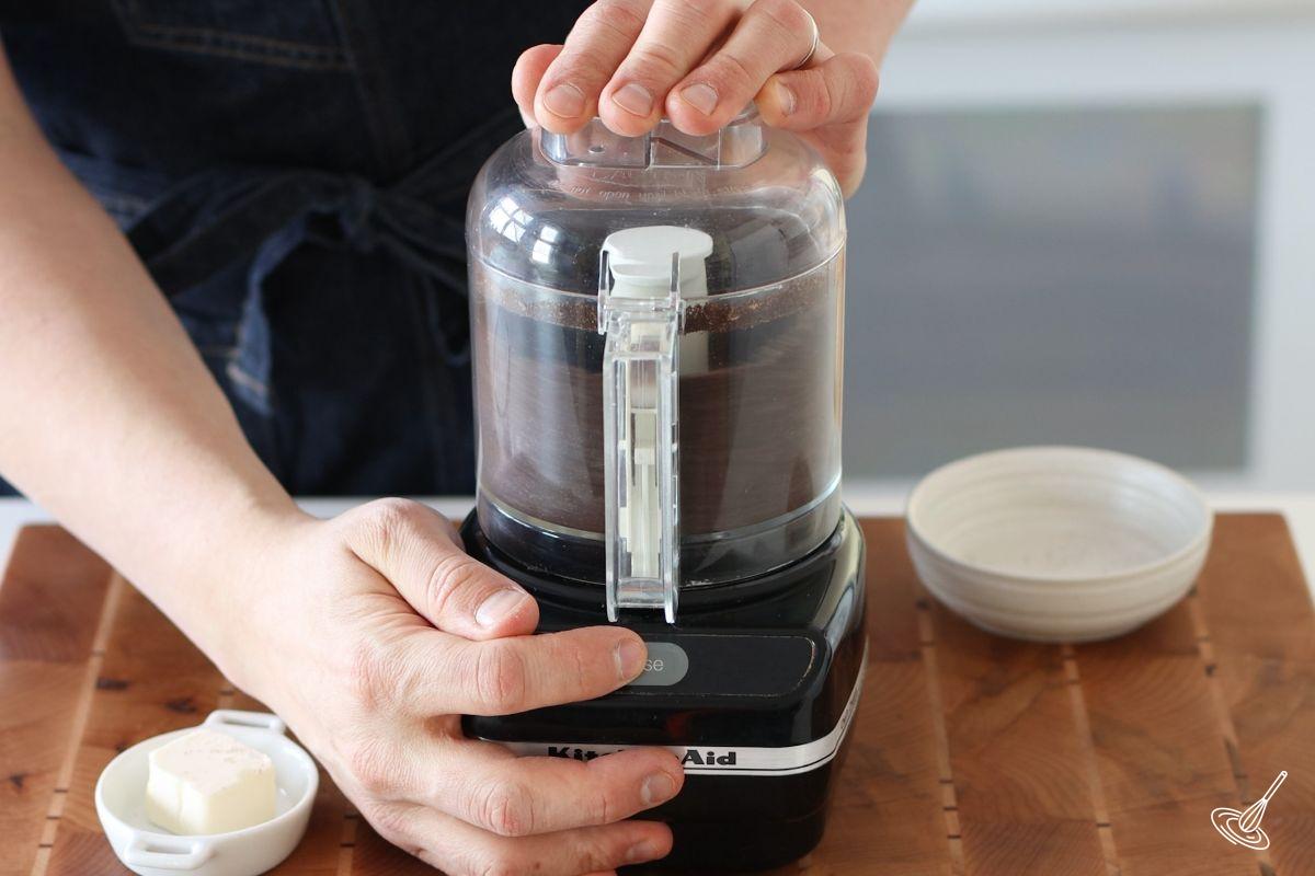 Someone using a small food processor to grind up chocolate sandwich cookies.