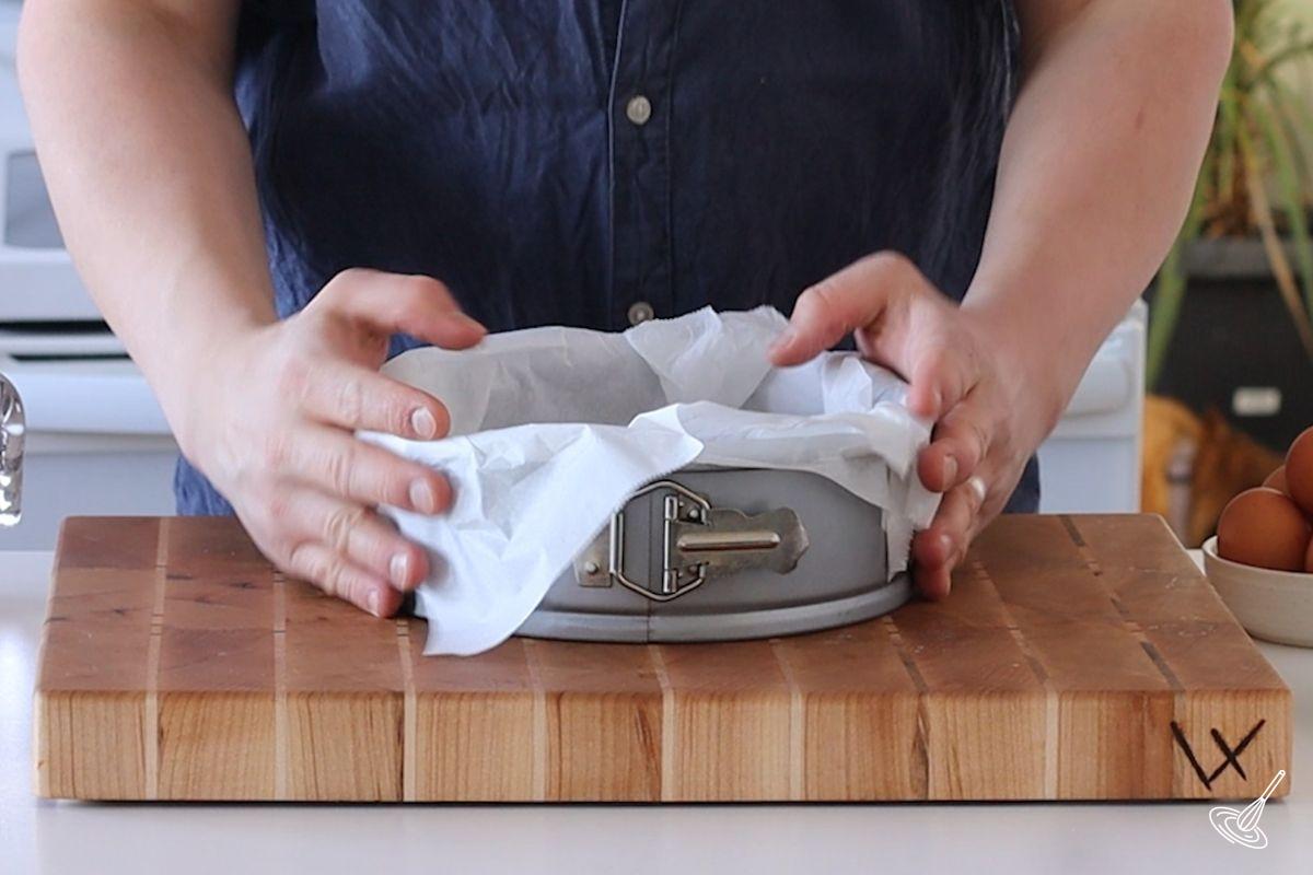 Someone lining a springform pan with parchment paper.