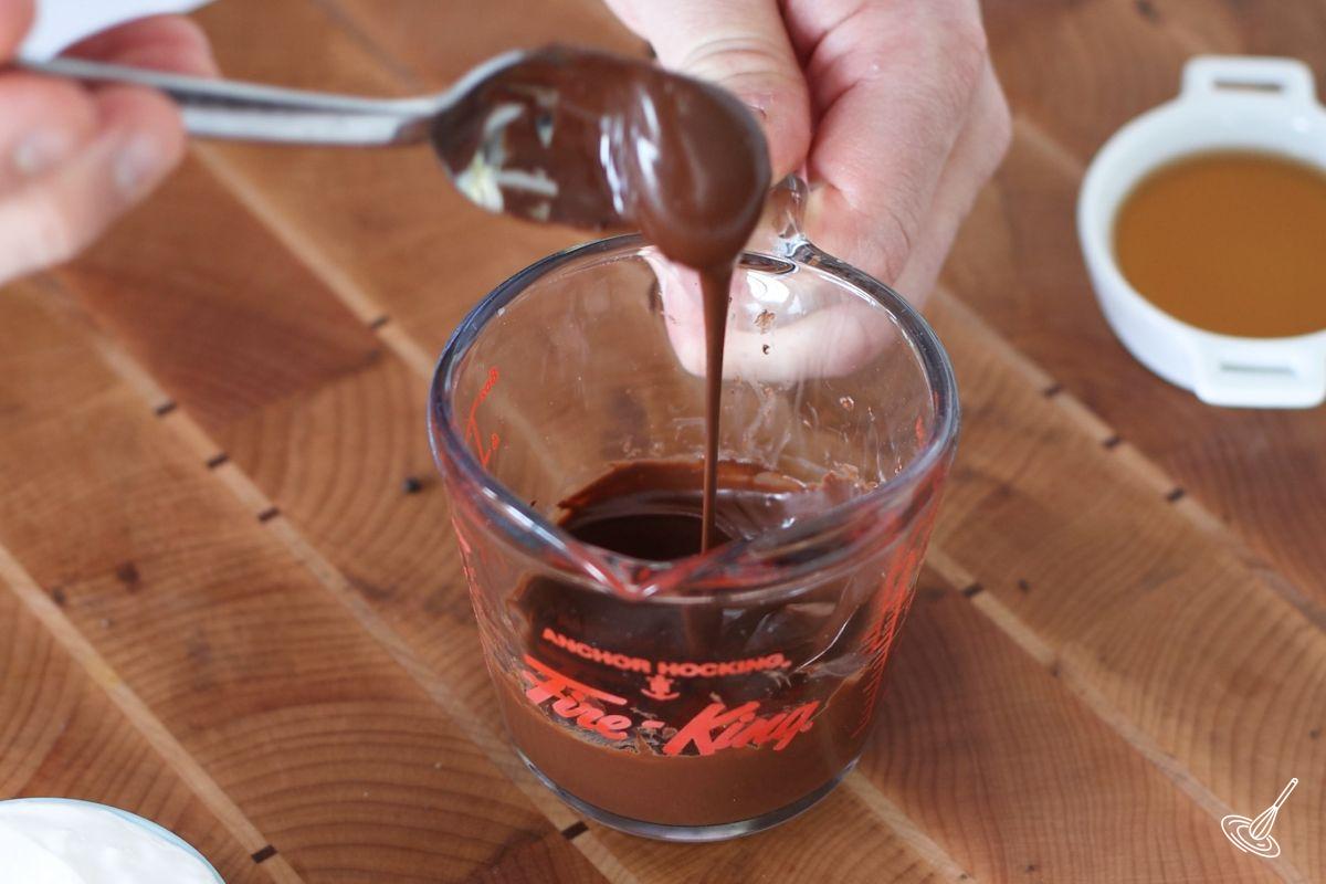 Someone using a small spoon to stir melted chocolate.