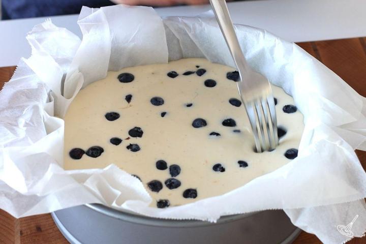 Someone using a fork to push blueberries into a cheesecake. 