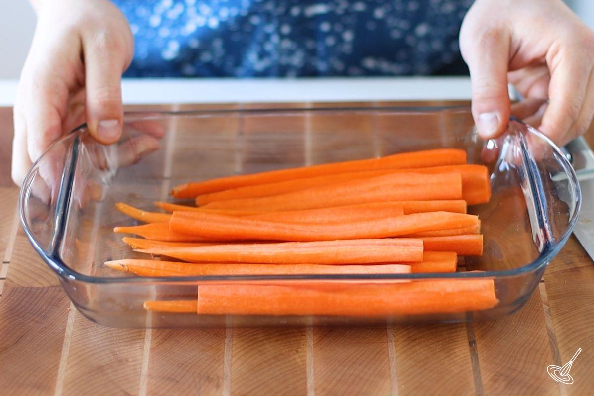 Peeled and halved carrots in a glass baking dish. 