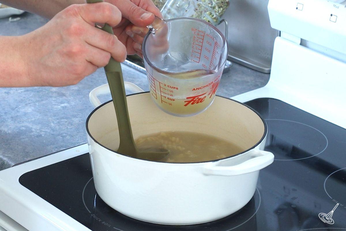 Someone using a soup ladle to take pasta water.
