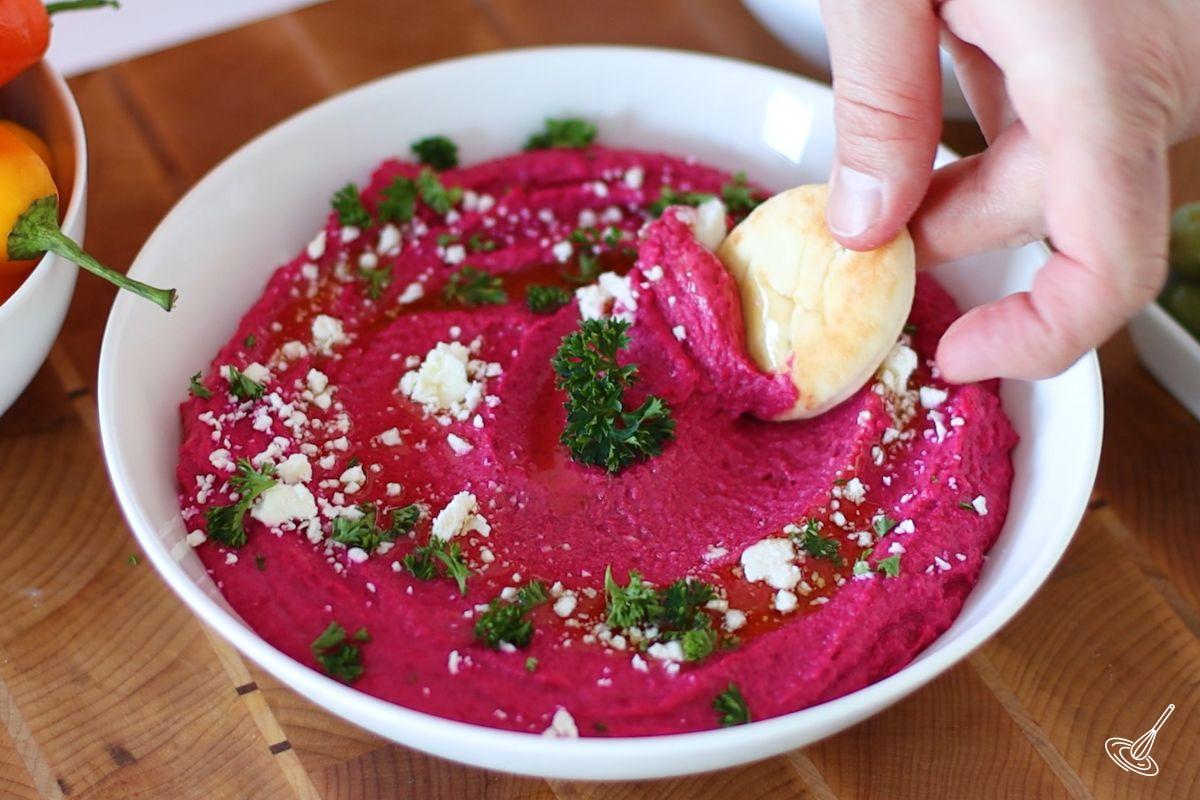 Someone using a mini naan bread to scoop up lemon beet hummus. 