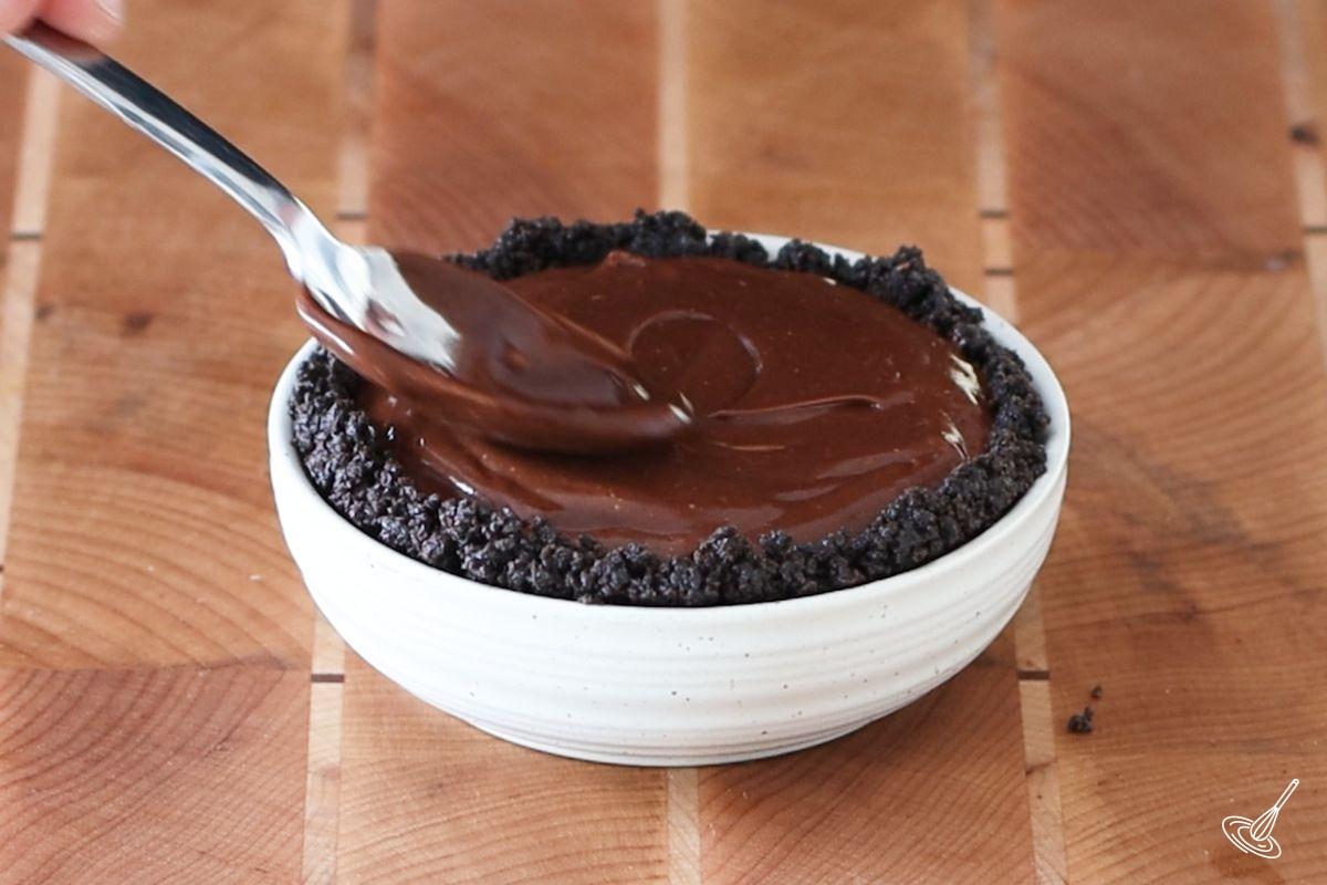 Someone using a spoon to smooth out the top of the Banana Chocolate Tart. 