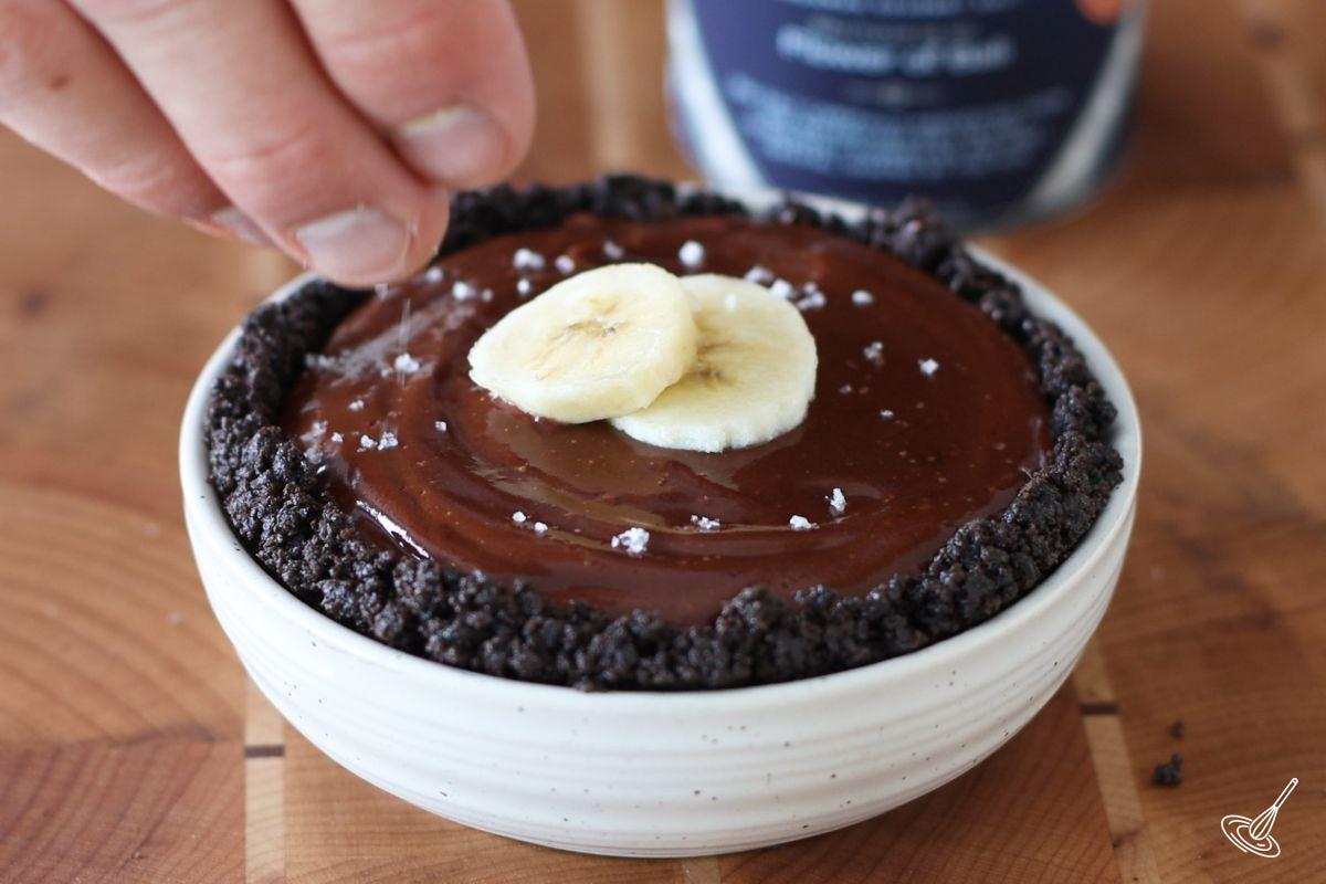 Someone sprinkling flaky sea salt on top of a Banana Chocolate Tart.