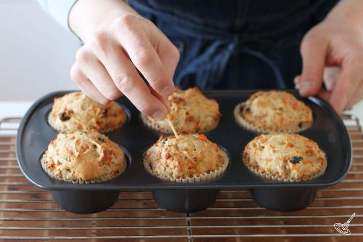 Someone using a toothpick to check the doneness of baked Carrot Cottage Cheese Muffins.