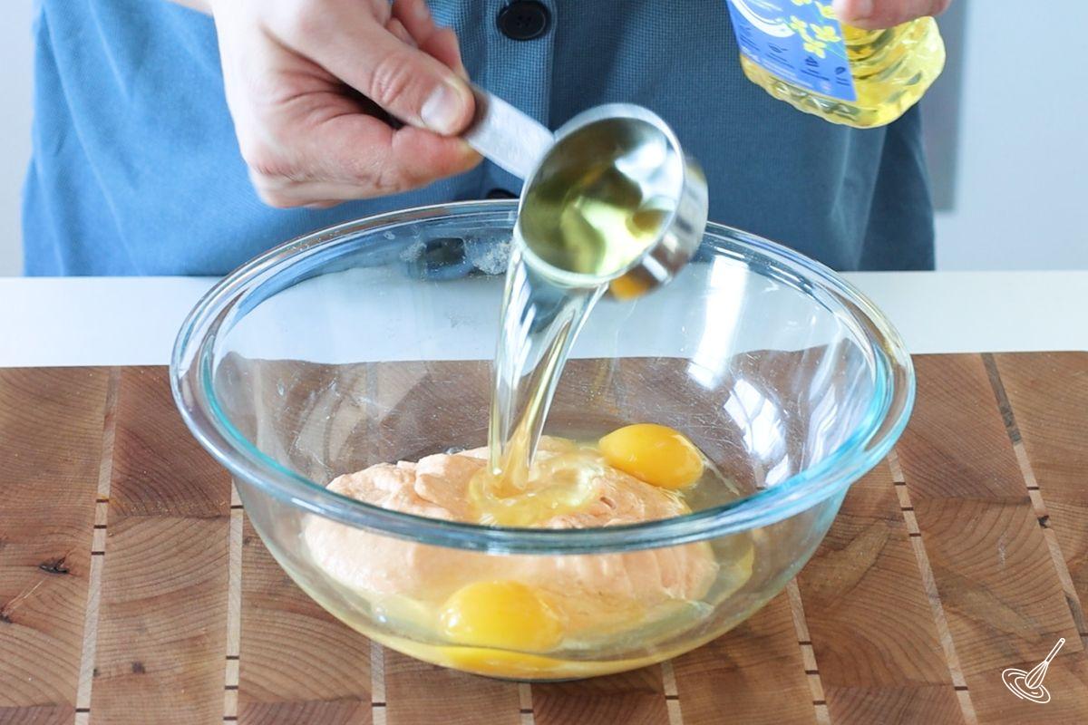 Someone adding canola oil to a large bowl of eggs and pumpkin. 