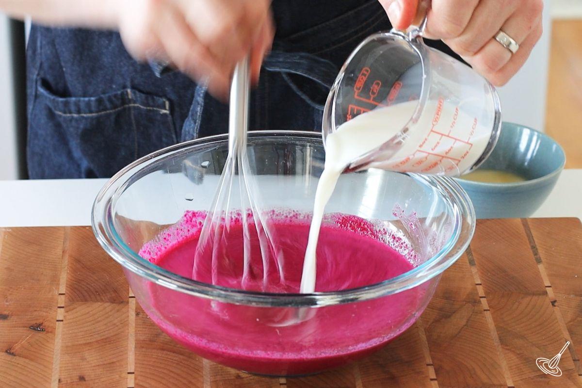 Someone whisking milk into a large bowl of puree beets.