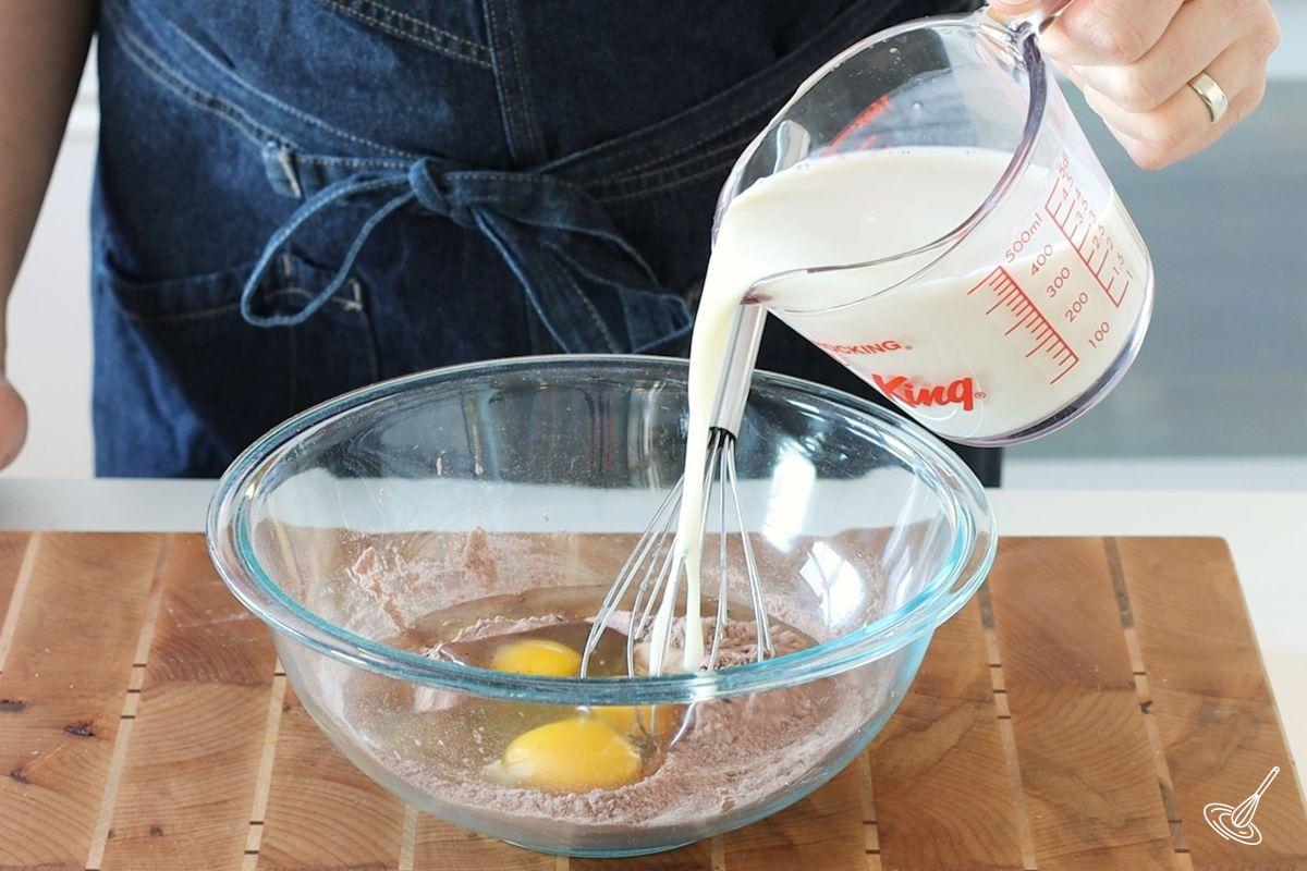 Someone pouring milk in a bowl with eggs.