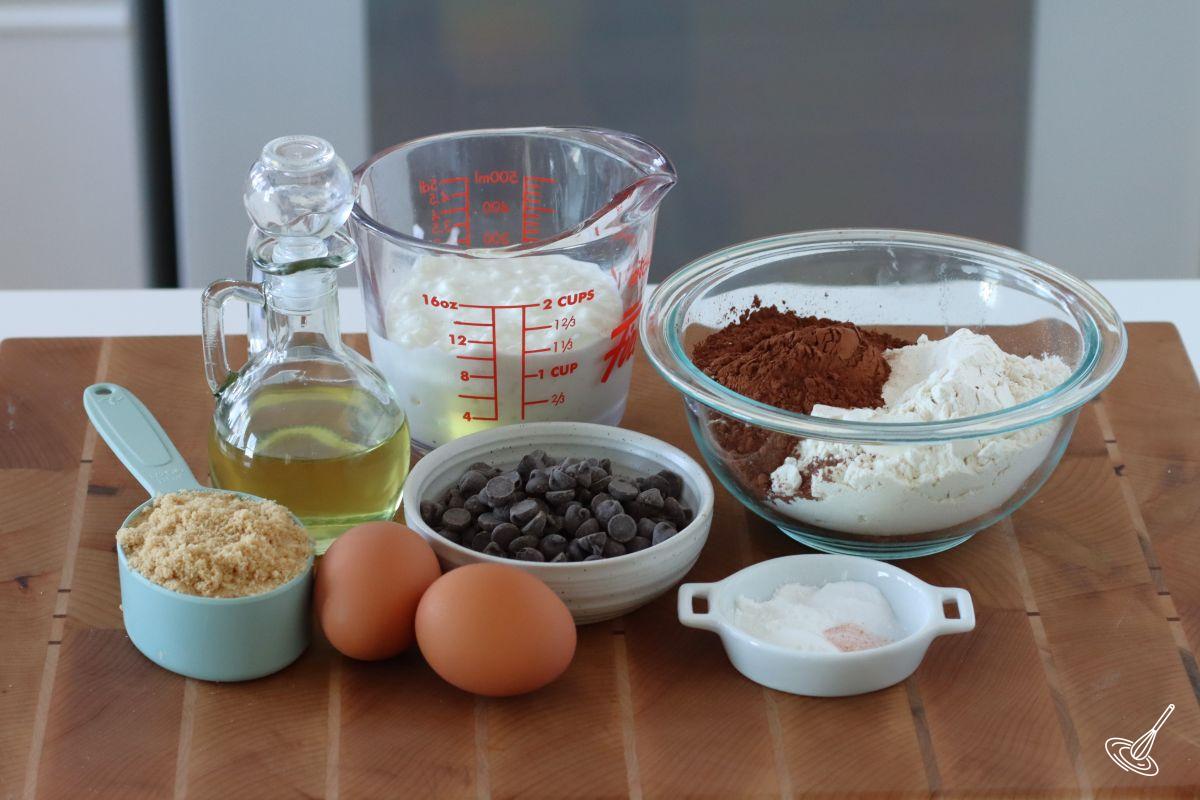 Ingredients on the kitchen counter, including flour, cocoa powder, chocolate chips, eggs, and sugar. 