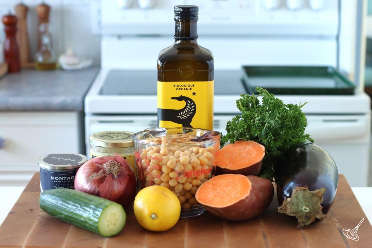 Ingredients on a cutting board, including chickpeas, aubergine, sweet potato, onion, and olive oil.