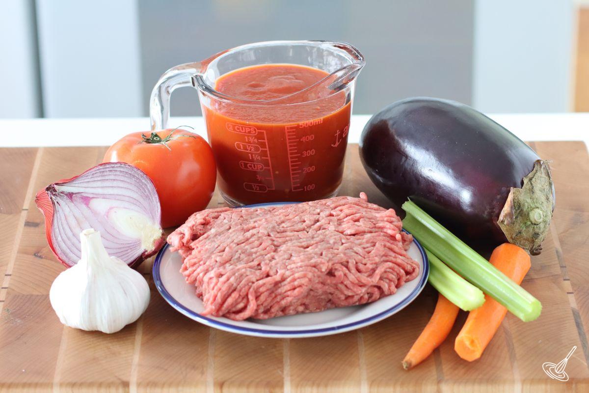 Ingredients on the counter including ground beef, aubergine, vegetables, and tomato sauce.