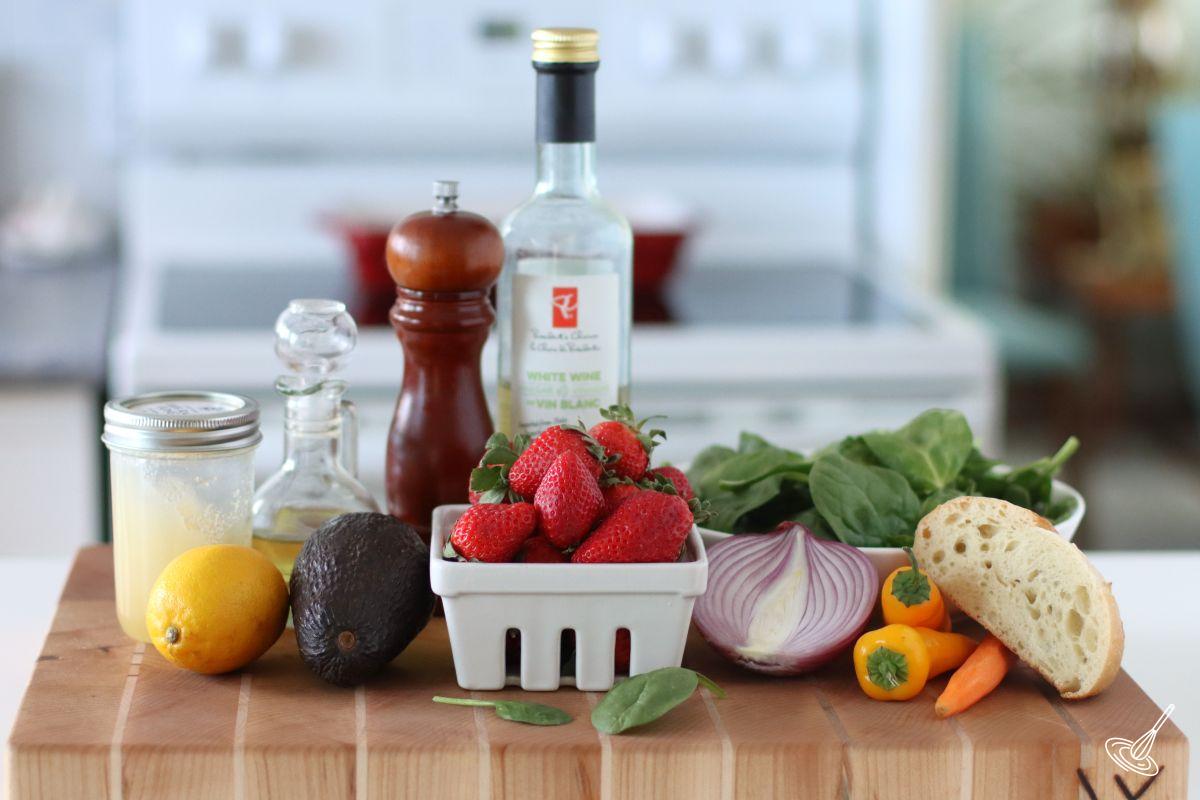 Ingredients on a cutting board including strawberries, onion, spinach, and avocado.