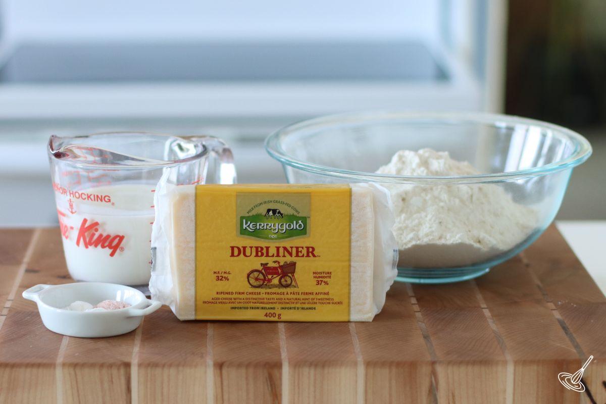 Ingredients on the kitchen counter including a bowl of flour, buttermilk, and a brick of cheese.