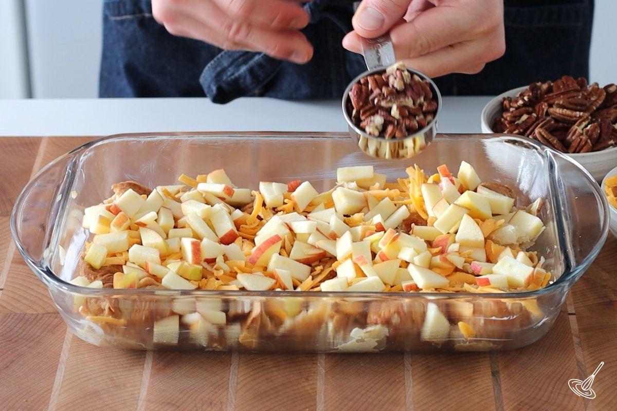 Someone sprinkling pieces of apple in a baking dish.